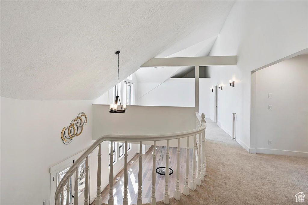 Hallway with a textured ceiling, carpet, an upstairs landing, and a notable chandelier