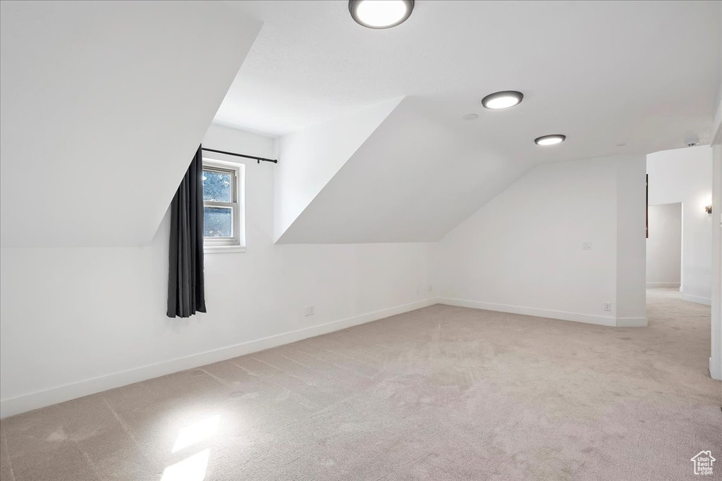 Additional living space with light carpet, vaulted ceiling, and baseboards