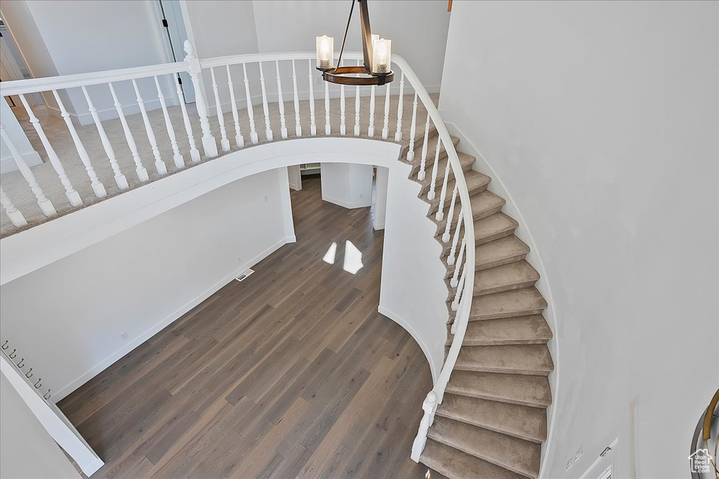 Staircase with arched walkways, wood finished floors, and an inviting chandelier