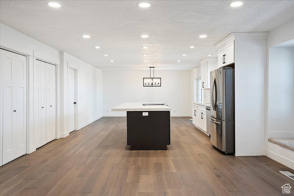 Kitchen with light countertops, freestanding refrigerator, white cabinetry, a kitchen island, and wood finished floors