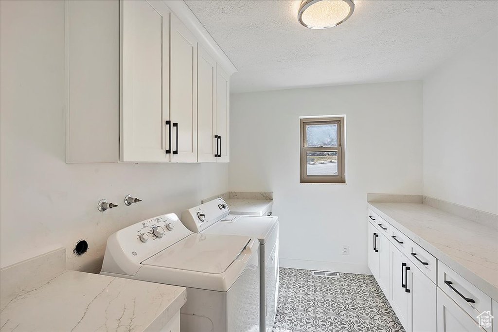 Clothes washing area featuring cabinet space, light tile patterned floors, baseboards, independent washer and dryer, and a textured ceiling