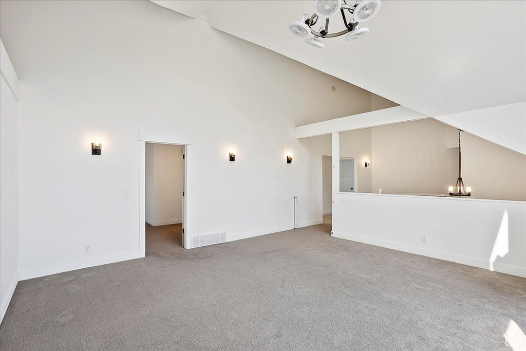 Unfurnished living room featuring high vaulted ceiling, carpet floors, visible vents, baseboards, and an inviting chandelier
