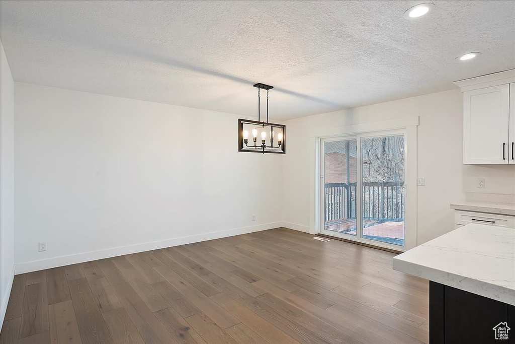 Unfurnished dining area with a notable chandelier, recessed lighting, dark wood-type flooring, a textured ceiling, and baseboards