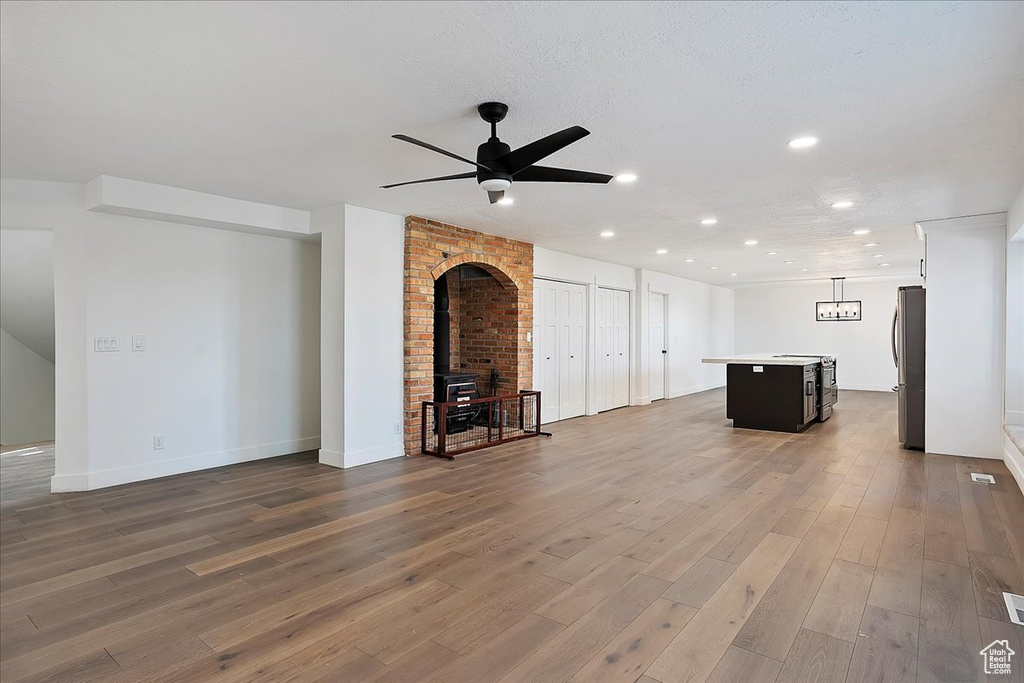 Unfurnished living room with recessed lighting, a wood stove, ceiling fan, wood finished floors, and baseboards