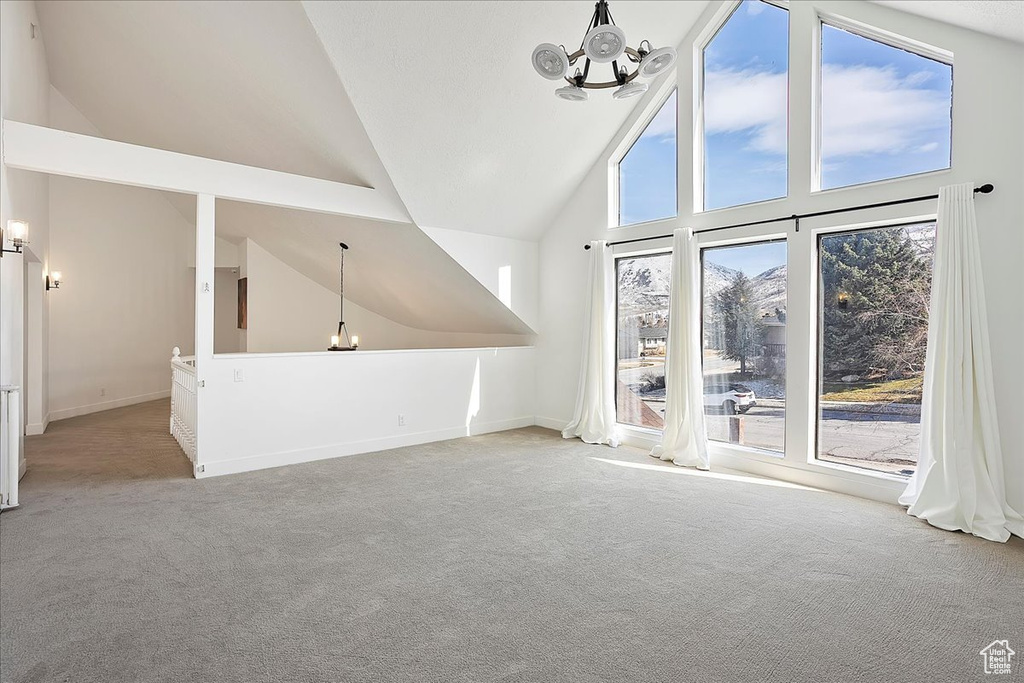 Unfurnished living room featuring carpet floors, high vaulted ceiling, baseboards, and an inviting chandelier