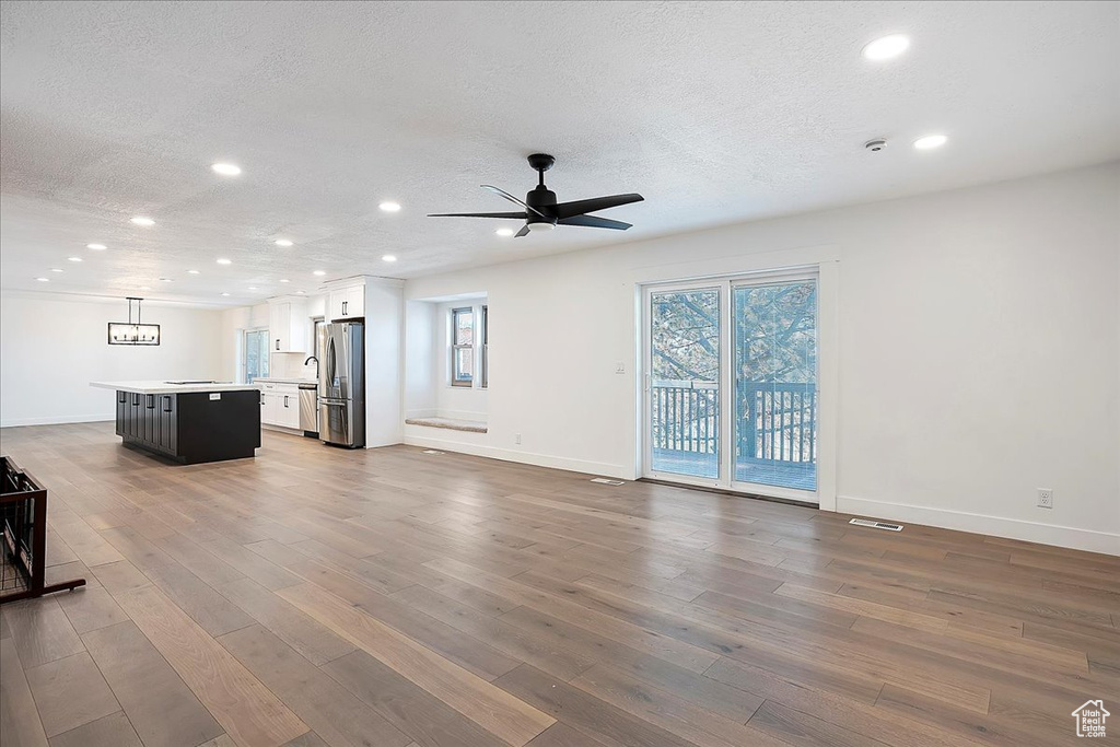 Unfurnished living room with a textured ceiling, wood finished floors, and a wealth of natural light