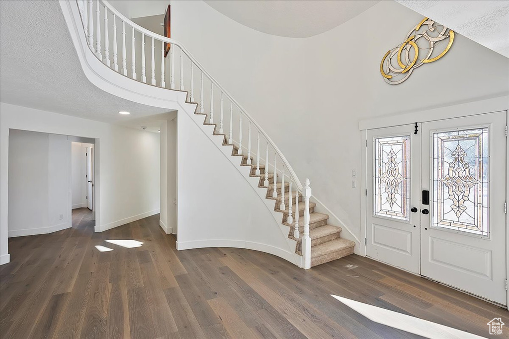 Foyer with baseboards, a towering ceiling, wood finished floors, stairs, and french doors
