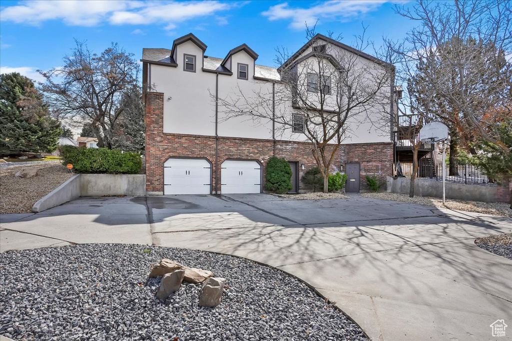 View of front of property featuring driveway, brick siding, an attached garage, and stucco siding