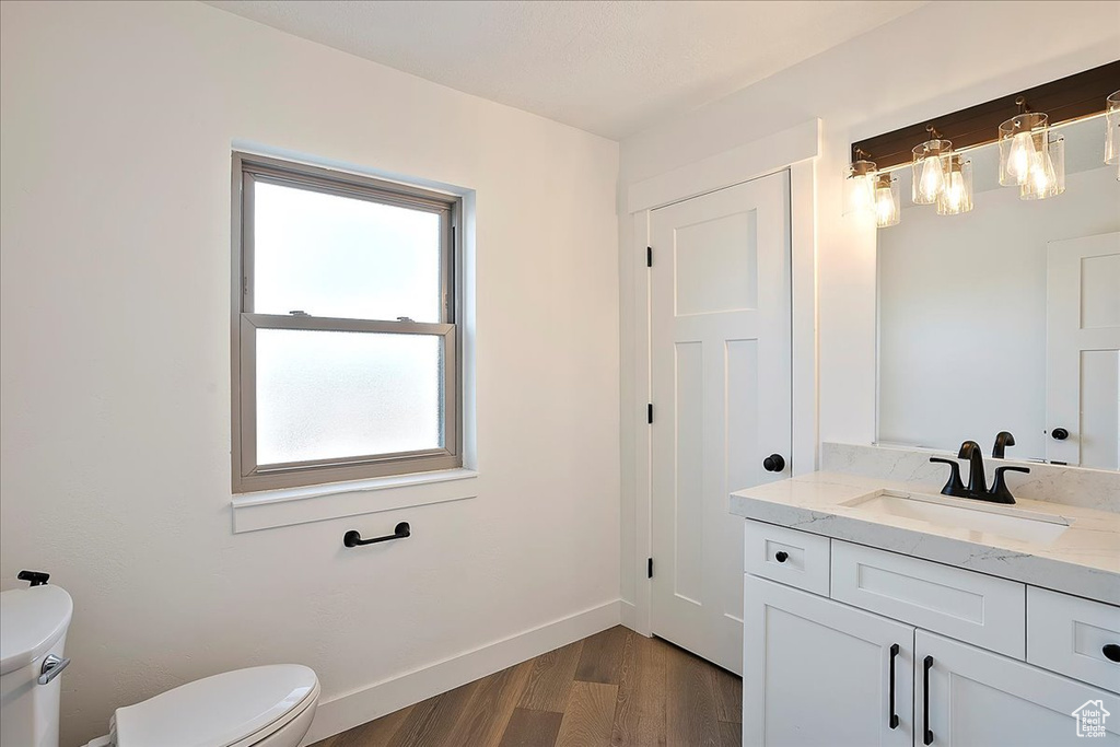 Half bath featuring baseboards, vanity, toilet, and wood finished floors