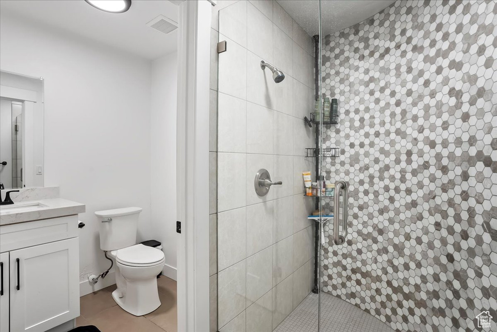 Bathroom featuring toilet, visible vents, vanity, tiled shower, and tile patterned floors