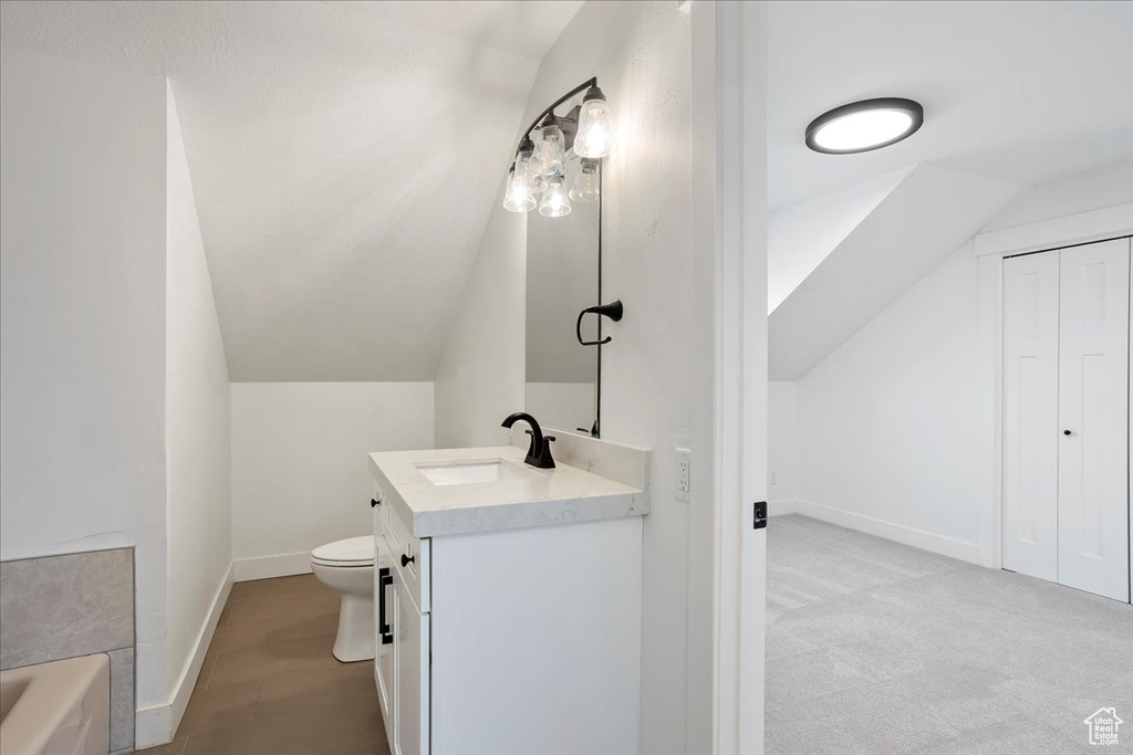 Full bathroom featuring toilet, vaulted ceiling, vanity, and baseboards
