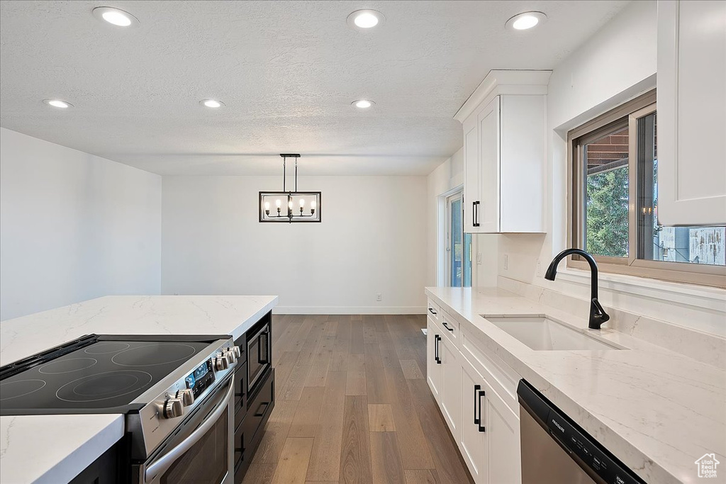 Kitchen featuring light stone counters, wood finished floors, a sink, white cabinetry, and appliances with stainless steel finishes