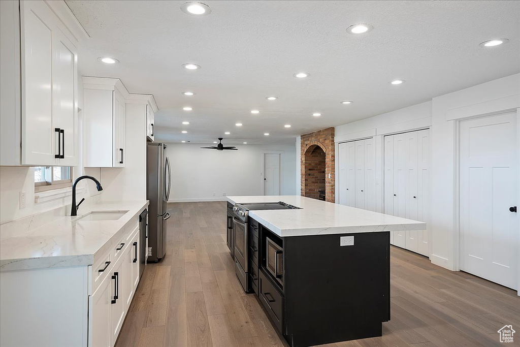 Kitchen with arched walkways, stainless steel appliances, light wood-style floors, white cabinetry, and a sink