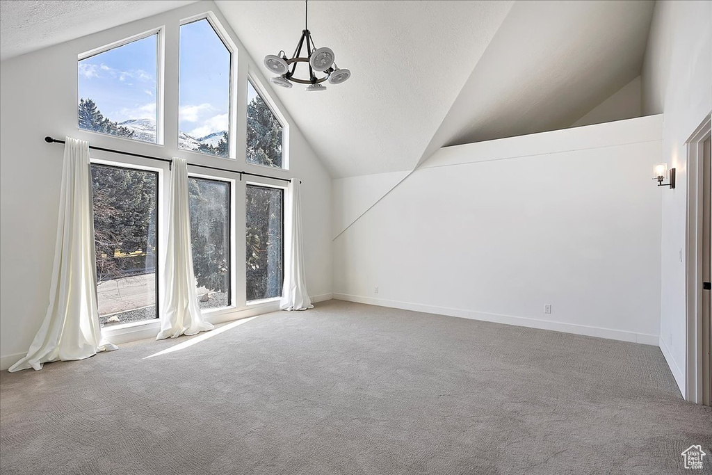 Unfurnished room with baseboards, high vaulted ceiling, carpet flooring, and a notable chandelier