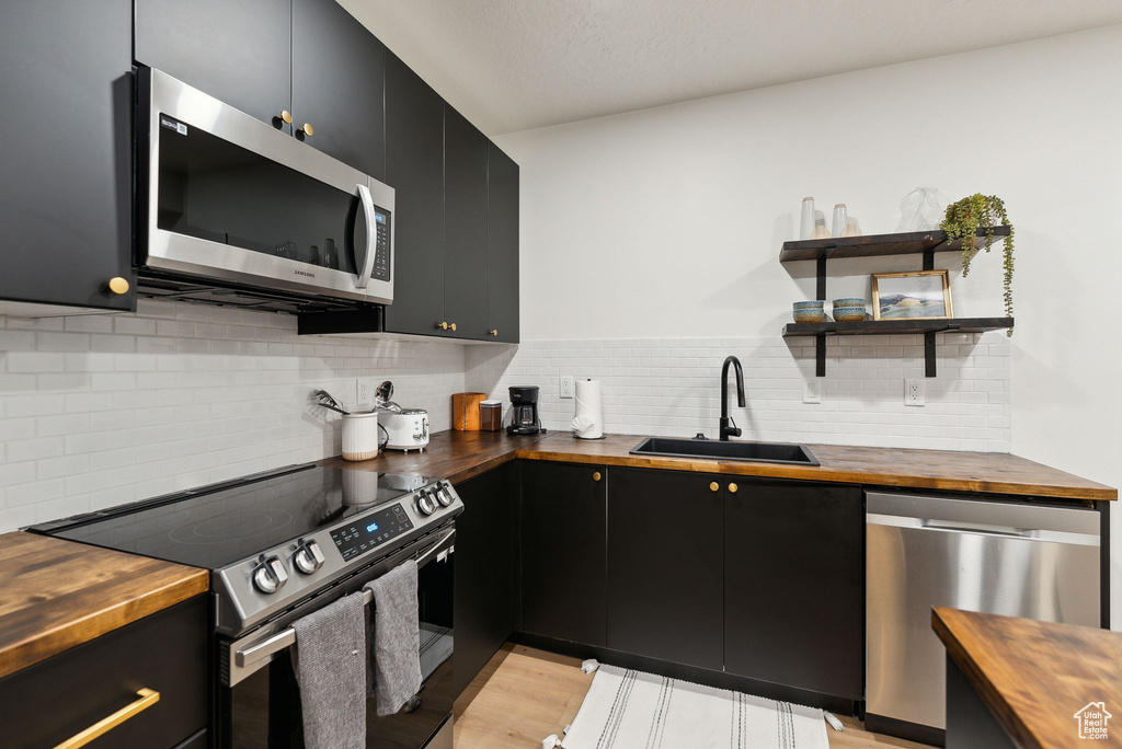 Kitchen with appliances with stainless steel finishes, dark cabinets, a sink, and wood counters