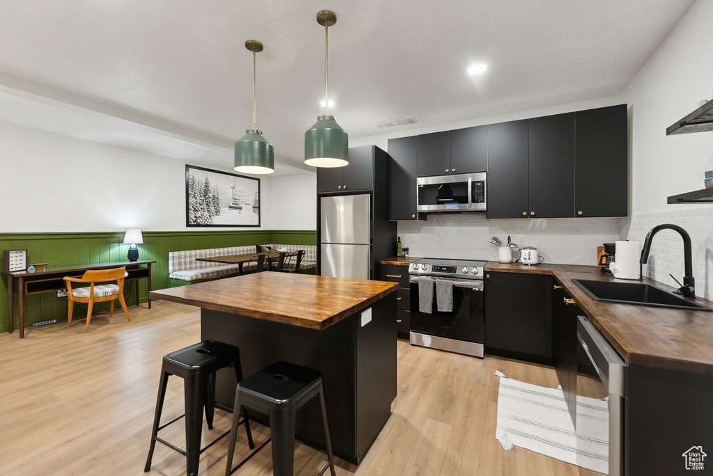 Kitchen with stainless steel appliances, butcher block counters, a sink, and dark cabinets