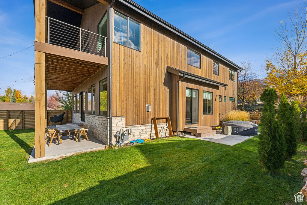 Back of house with a lawn, a patio area, fence, a balcony, and stone siding