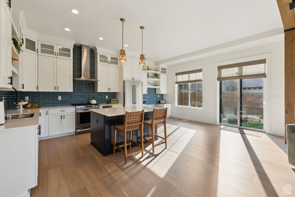 Kitchen with stainless steel appliances, wall chimney exhaust hood, light countertops, and backsplash