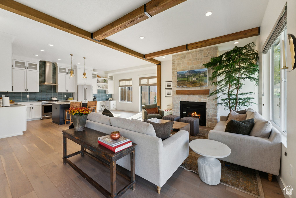 Living area with beam ceiling, recessed lighting, a stone fireplace, wood finished floors, and baseboards
