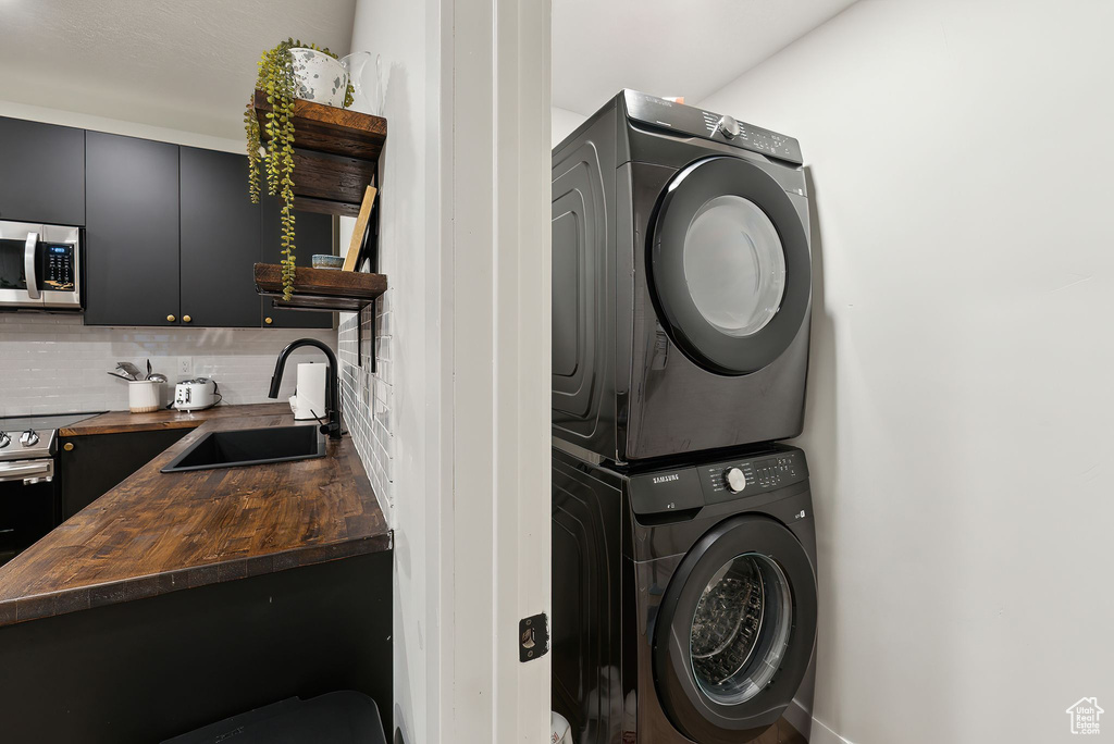 Clothes washing area featuring stacked washing maching and dryer and a sink