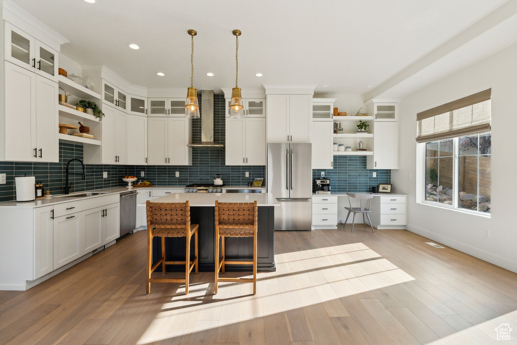 Kitchen featuring appliances with stainless steel finishes, a sink, wall chimney exhaust hood, and open shelves
