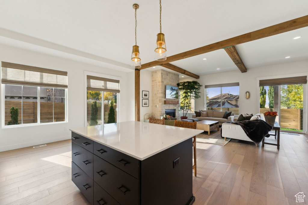 Kitchen with light wood finished floors, beamed ceiling, dark cabinetry, a fireplace, and pendant lighting