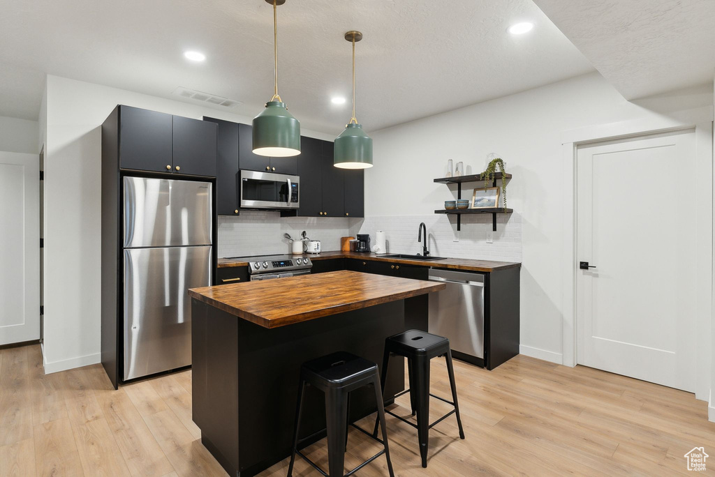 Kitchen featuring light wood-style floors, butcher block counters, stainless steel appliances, and a sink