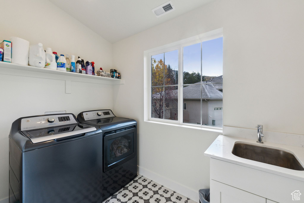 Clothes washing area with washing machine and dryer, laundry area, a sink, visible vents, and baseboards