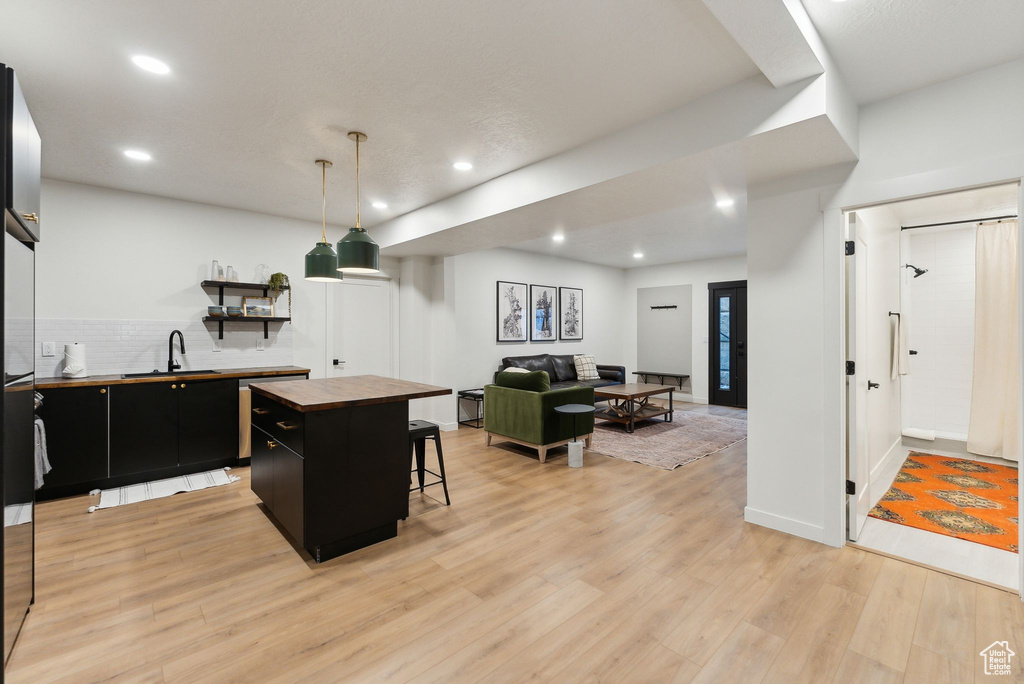 Kitchen with butcher block counters, light wood-style flooring, dark cabinets, a center island, and a sink