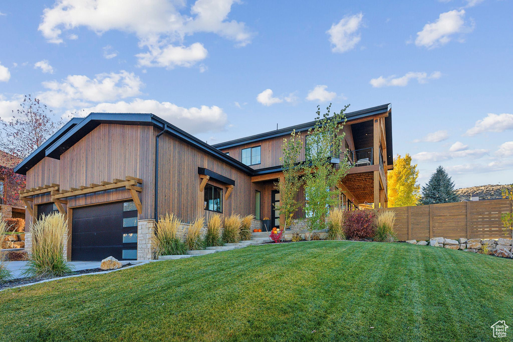 View of front facade featuring a front yard, stone siding, fence, and an attached garage