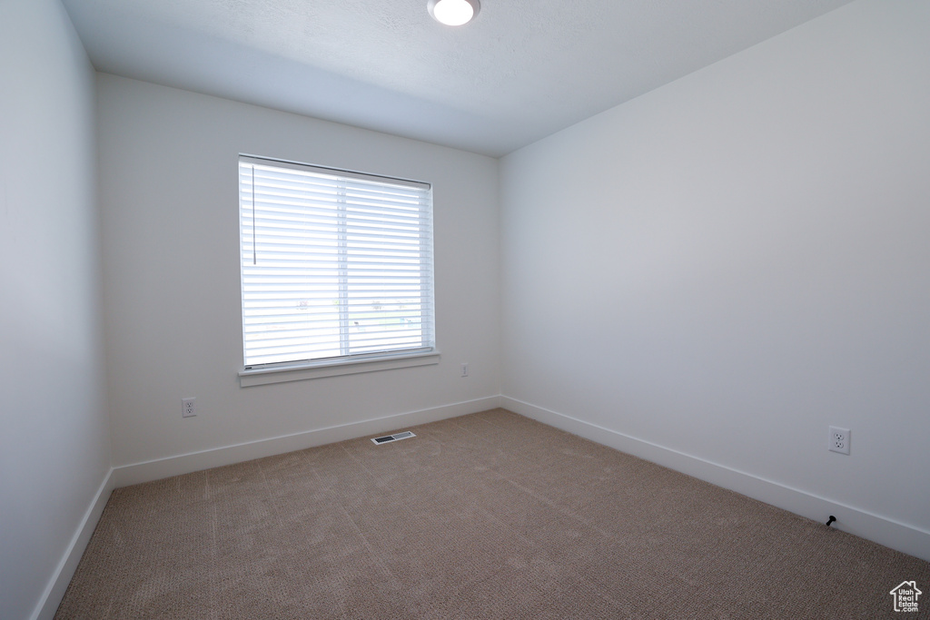 Empty room featuring light carpet, visible vents, and baseboards