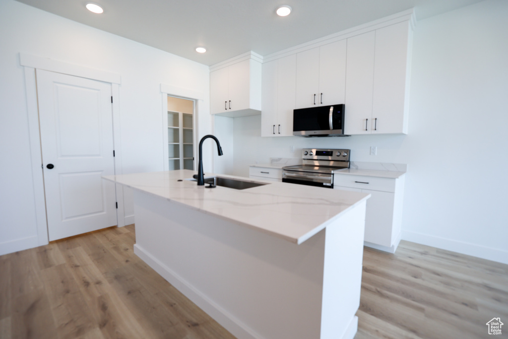 Kitchen with stainless steel appliances, a sink, a kitchen island with sink, and white cabinetry