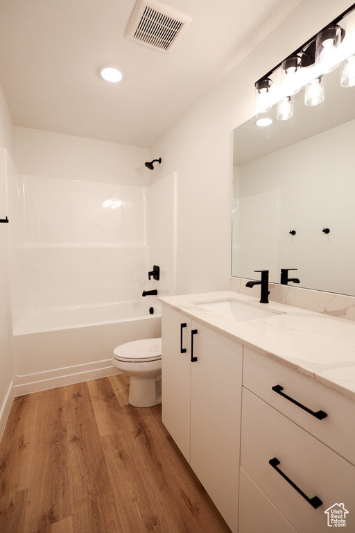 Full bath featuring visible vents, toilet, vanity, shower / tub combination, and wood finished floors
