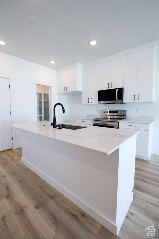 Kitchen featuring an island with sink, stainless steel appliances, light wood-style floors, white cabinetry, and a sink