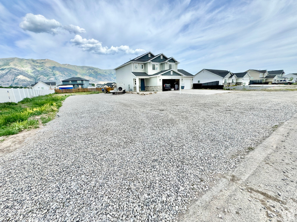 View of front of house with driveway, a mountain view, stone siding, an attached garage, and a residential view