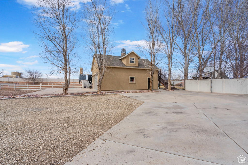 View of side of property featuring roof with shingles, a chimney, stucco siding, fence, and driveway