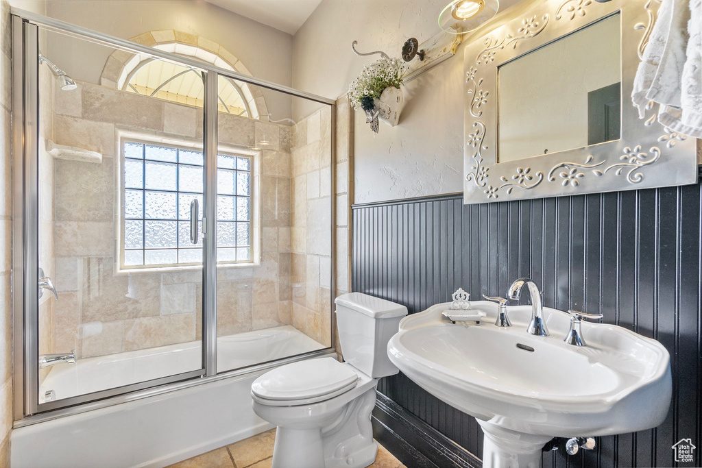 Bathroom featuring bath / shower combo with glass door, toilet, wainscoting, a sink, and tile patterned flooring