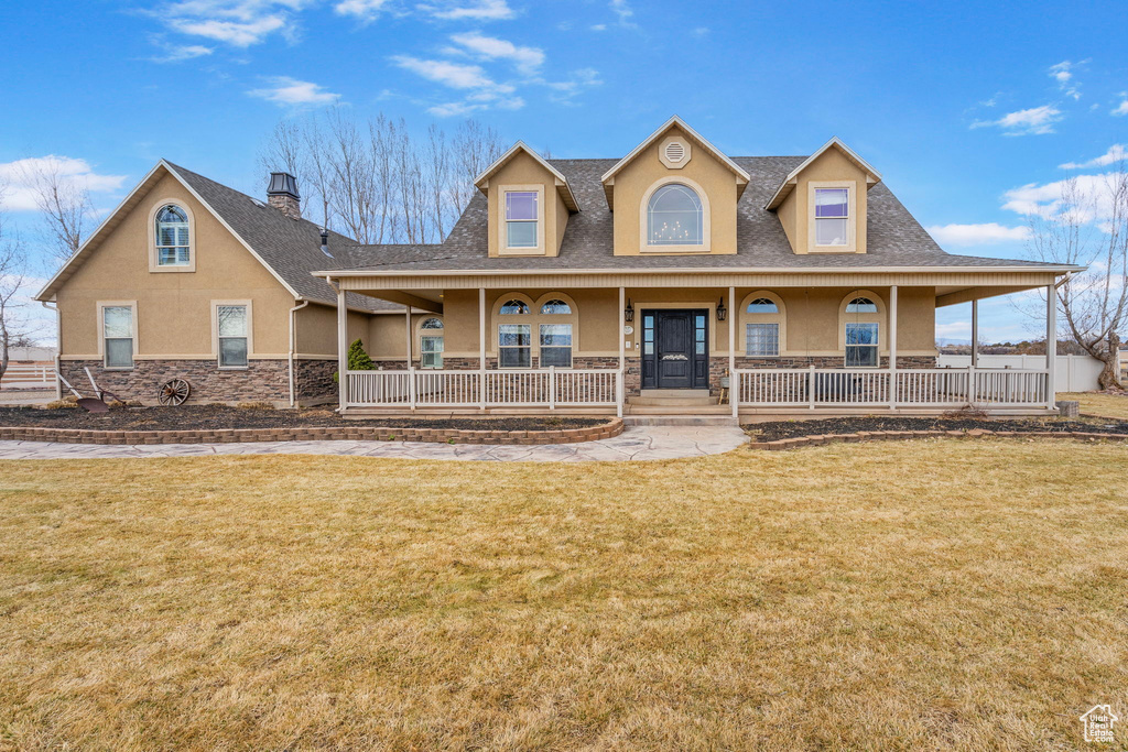 View of front of property featuring covered porch, a shingled roof, stone siding, stucco siding, and a front lawn