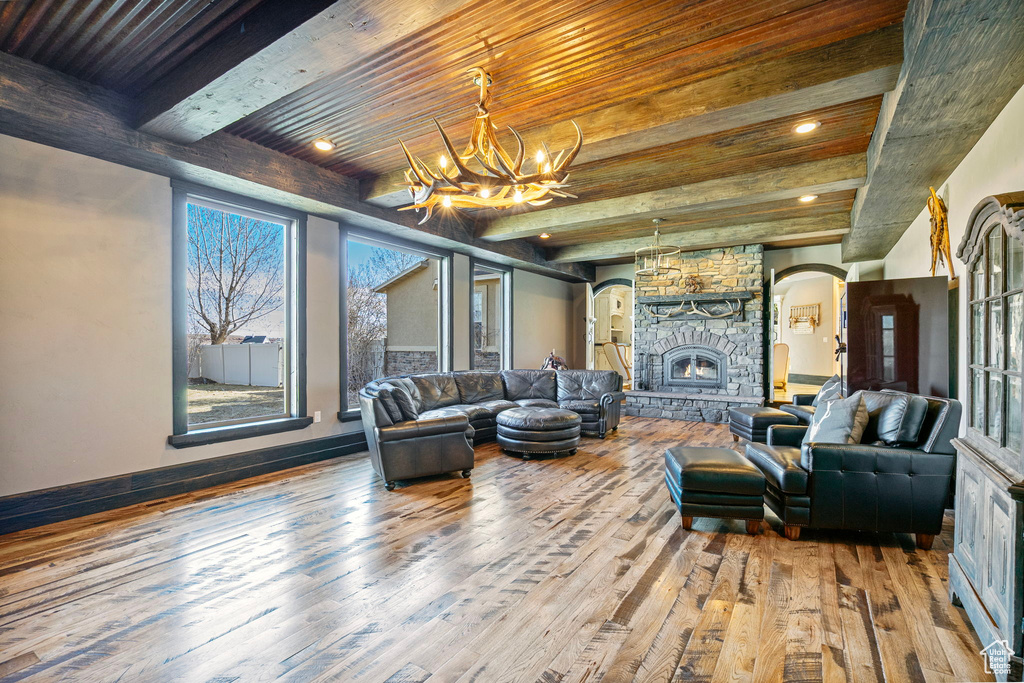 Living area with wood-type flooring, an inviting chandelier, a stone fireplace, beamed ceiling, and baseboards