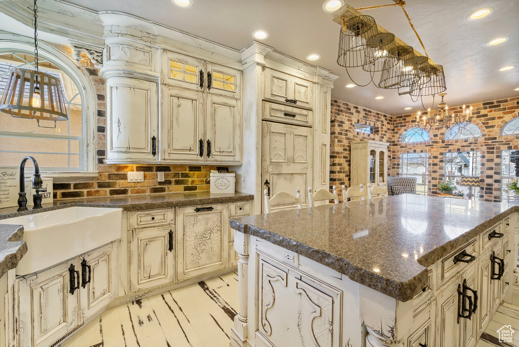 Kitchen featuring a chandelier, brick wall, a sink, and cream cabinets