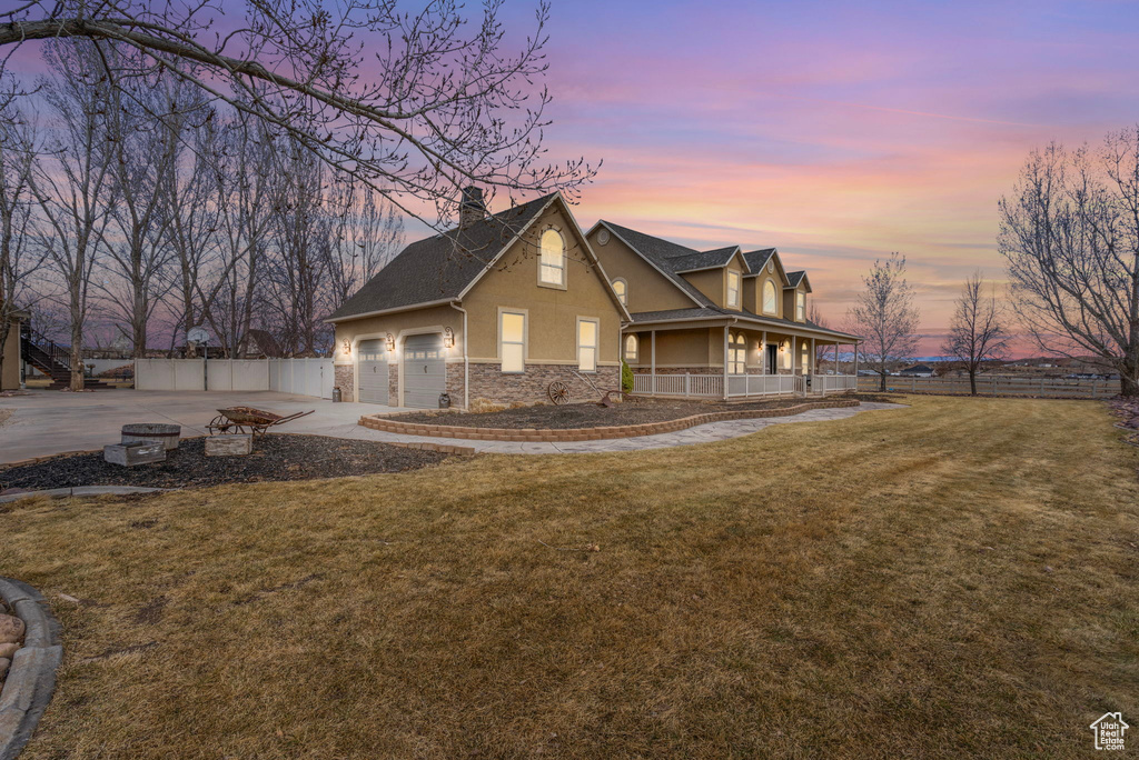 View of front facade featuring stucco siding, covered porch, a front yard, fence, and stone siding