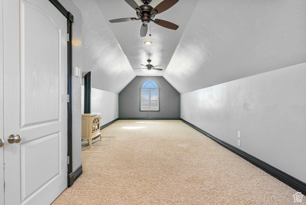 Bonus room with lofted ceiling, a ceiling fan, baseboards, carpet, and a wood stove