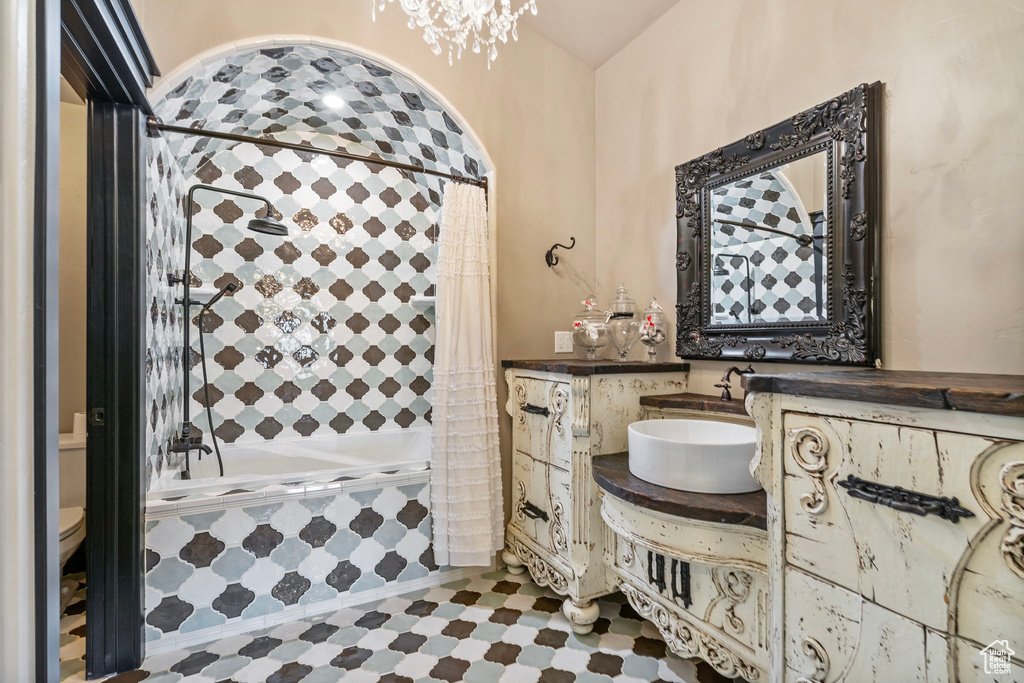 Full bathroom featuring toilet, tiled shower / bath combo, a chandelier, and vanity