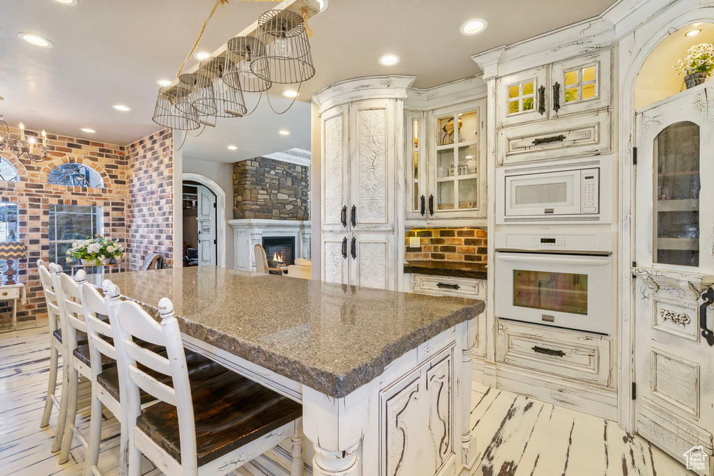 Kitchen featuring arched walkways, cream cabinets, white appliances, a kitchen island, and glass insert cabinets