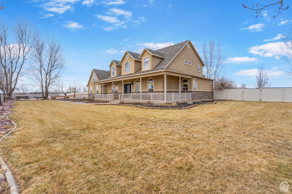 Farmhouse-style home with stucco siding, a front yard, a gate, fence, and stone siding