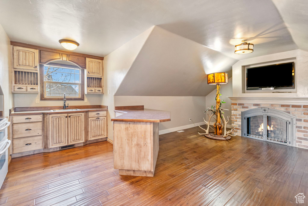 Kitchen with light brown cabinetry, a brick fireplace, a sink, and hardwood / wood-style flooring