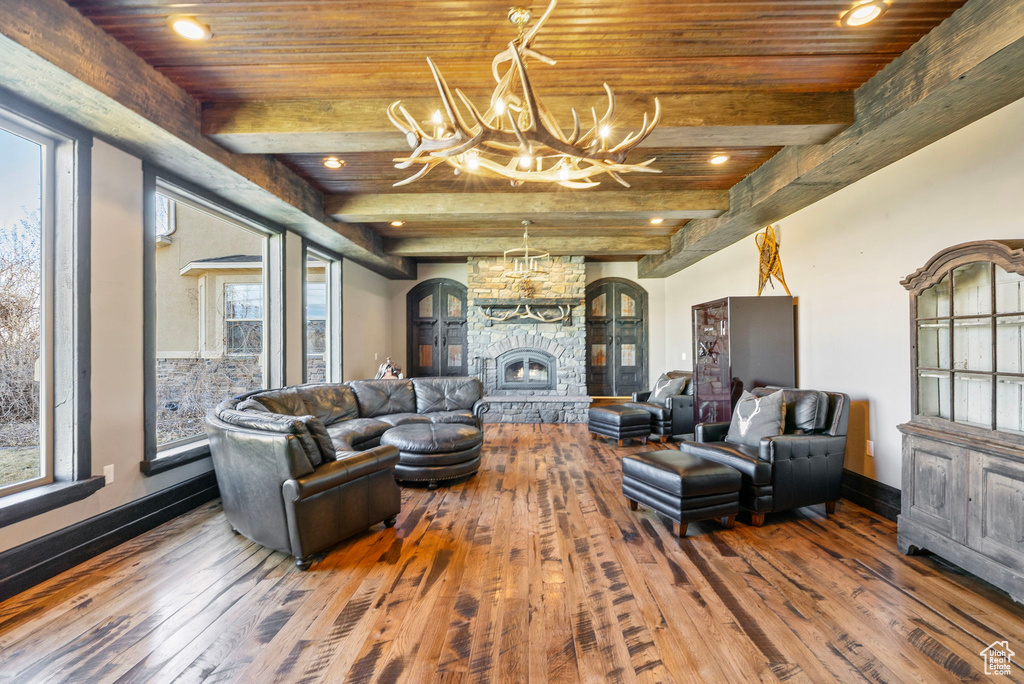 Living area featuring a stone fireplace, wooden ceiling, hardwood / wood-style flooring, a notable chandelier, and beam ceiling