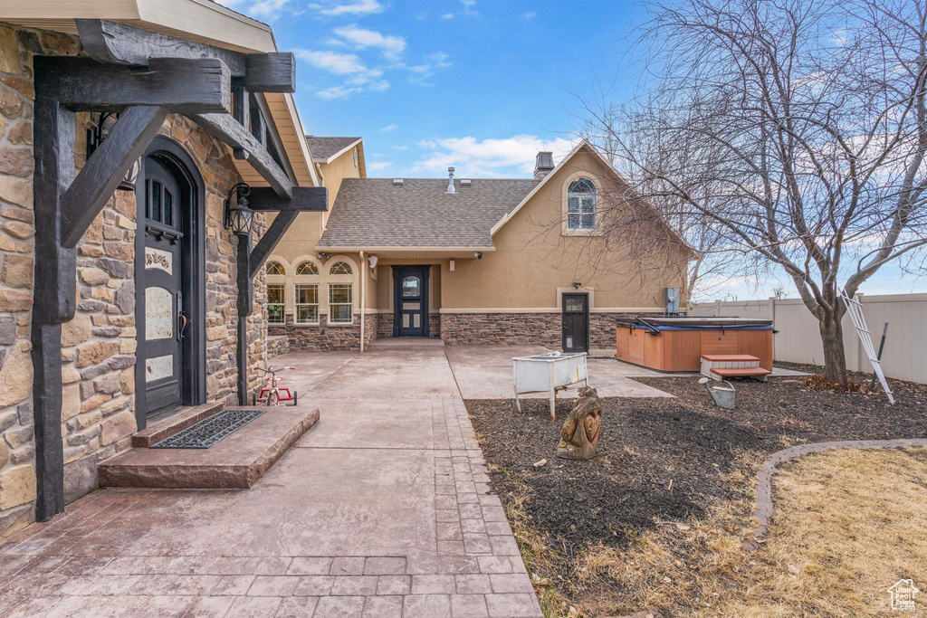 View of front of property featuring a hot tub, stone siding, roof with shingles, fence, and stucco siding