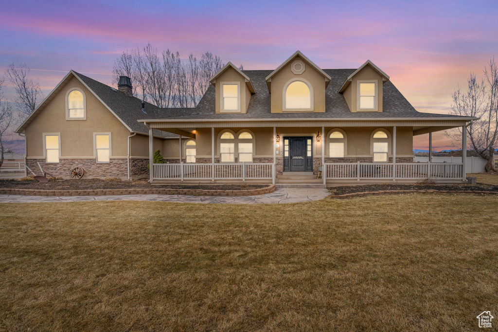 Country-style home with stone siding, a front lawn, a porch, and stucco siding