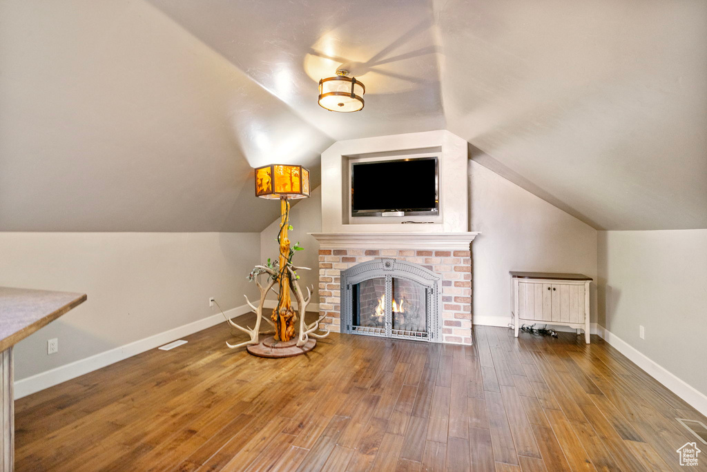 Unfurnished living room with lofted ceiling, a brick fireplace, baseboards, and wood finished floors